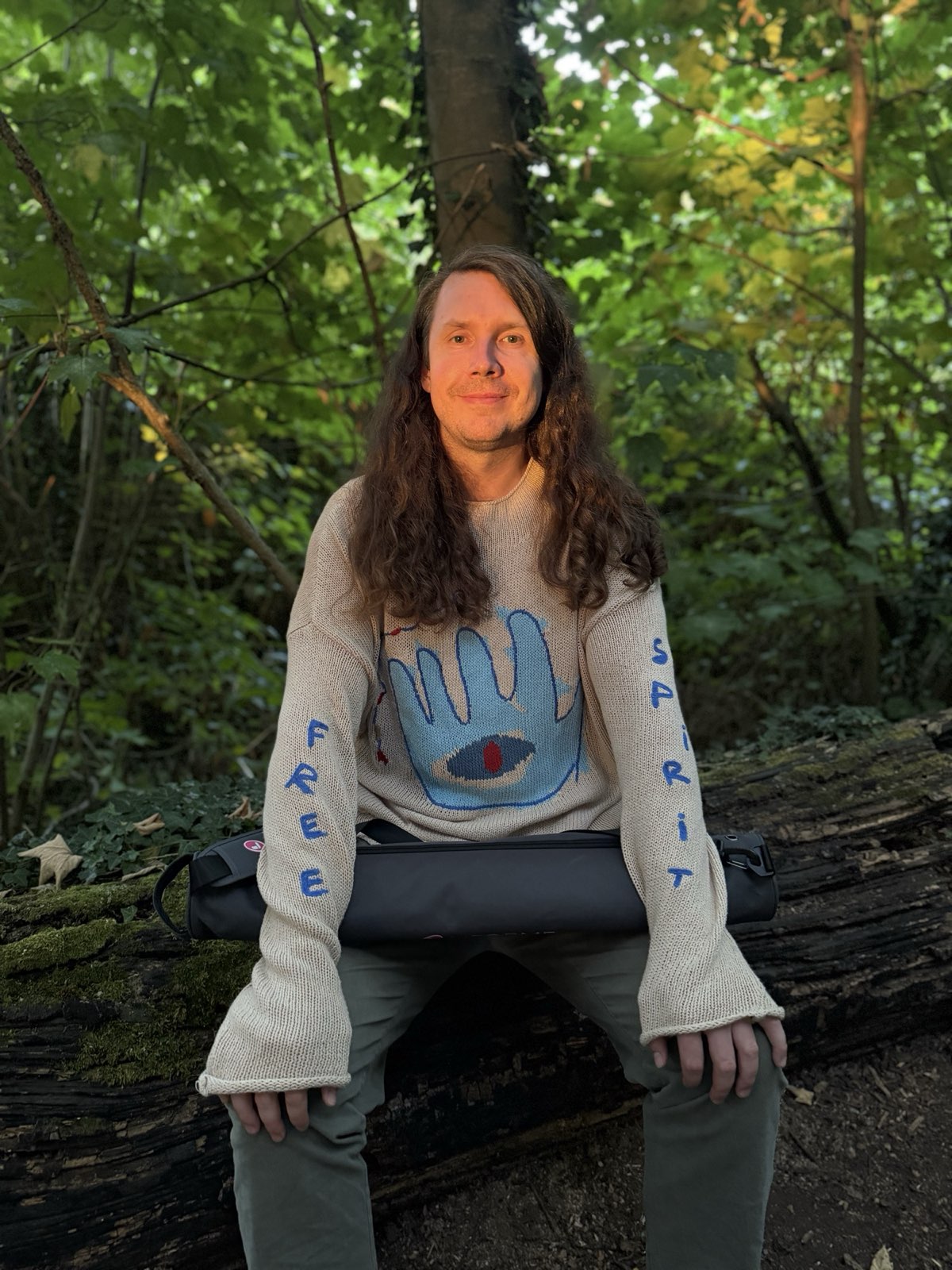 Ben smiling, seated with a rolled yoga mat, outdoors in evening light